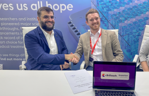2 men shaking hands, looking at the camera and smiling with signed contract in front of them