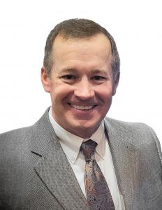 An image of Rob Neal in a suit in front of a white background, smiling at the camera.