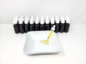 a row of 1 ounce oil bottles with droppers and lids lined up with one bowl in front and one dropper in the bowl showing the color of the liquid
