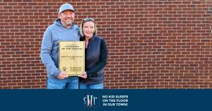 Scott and Lisa Foster standing in front of a brick wall holding the Guardian of the Mission award they just received