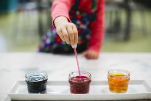 Child dips brush into red colored paint in the Children's Museum of Tacoma Studio