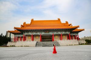 Christine walks in a red dress that is similar to the colors of the pillars of the National Theatre and Concert Hall in Taipei behind her.