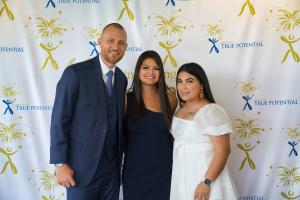 Ross Pesek and Karen Pesek are pictured with Lesvia Marroquin, the first True Potential Scholar to complete her associate's degree and go on to her bachelor's degree with help from the program. They are in formal clothing and pictured in front of the True