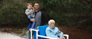 A man carrying a little boy, and an elderly woman sitting on a white chair.