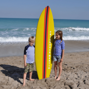 A young boy and a young girl standing next to a surf paddle in a beach.