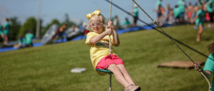 A young white girl wearing spectacles on a swing.