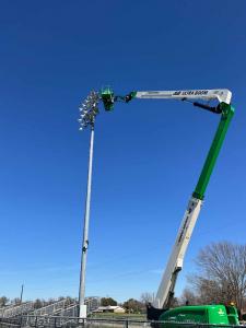 Crane elevated next to outdoor athletic lighting, in the process of upgrading existing lights to modern LED light fixtures.