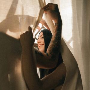 A smiling woman and her partner are partially obscured by a curtain.