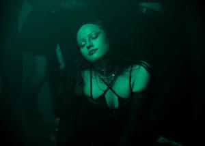 A photo of Xaya dancing freely behind the scenes of the "Walk Away" music video. She is in a club setting with green fluorescent lights highlighting her movement. Her stunning makeup, courtesy of Lea Reitberger while her outfit by Manure de Voir.