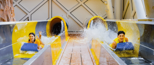 An Asian female and an Asian male are enjoying water slides at Studio City Macau, each on one side.