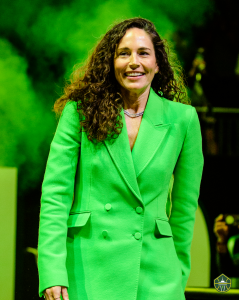 Sue Bird standing on basketball court in business suit.