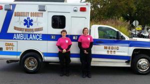 Photo of EMT Kristie Parrill and Paramedic Courtney, both in black pants and lavender EMS T-Shirts, standing in front of the ambulance they used during the rescue.  The ambulance is white with blue trim and markings.