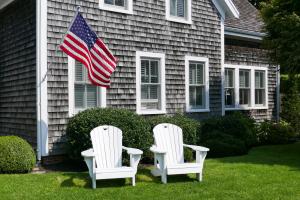 Two Adirondack chairs in front of a wooden house with US flag