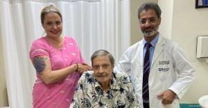 3 people including one doctor, and one person sitting down looking at camera.
