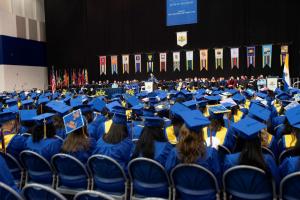 Students in caps and gowns watching speaker at commencement ceremony.