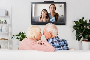 Older family enjoying a video call on TV with their daugher and grandkids