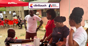 Group of people stood around a table, providing care to someone who is sat down and having their blood pressure taken