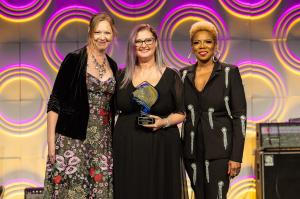 Portia Sabin (left) and Gina Miller (right) present Cameo Carlson (center) with the Music Biz 2024 Presidential Award for Outstanding Executive Achievement.