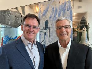 Photo of Chairman of the Board at GoGetIt, Shawn Horwitz (right), and the new CEO, Barend Venter (left), standing together in an indoor setting. Both are smiling warmly at the camera. Shawn is wearing a black suit and white shirt, while Barend is dressed 