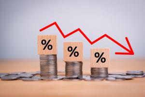 Percentage sign on wooden cubes with Stack of coin bar chart and red graph trending downwards on white background