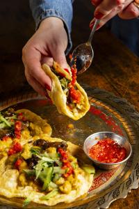 A person holding a folded double, adding hot sauce on it