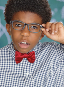 Young African American boy adjusting his blue glasses, wearing a gingham check shirt and a red bow tie, looking smart and confident. A shining example of the talent nurtured at The Industry Network.