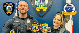 Two Merced Police Department officers in uniform proudly display their department patches in front of the Merced Police Department emblem.