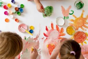 Close up image of 3 children using brushes to pain on a large piece of paper
