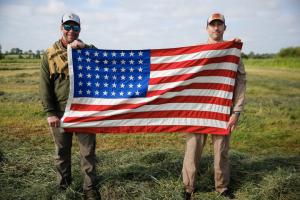 Kyle Daniels, Firebrand Founder (right), and Chase Millsap (left) holding a commemorative 48 star firebrand flag in the jump landing zone outside of Carentan, France.