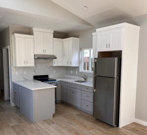 Photo inside of a modern ADU featuring from left to right a kitchen counter, oven/stove, sink, and refrigerator