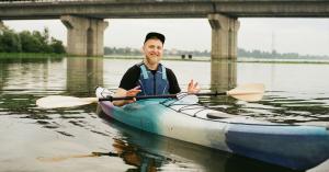 Male kayaker wearing a life jacket on calm water in front bridge abutment