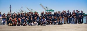 A large group of high school students who were a part of EXP Internship Program in the summer of 2023 standing on a dock. Behind them is the Port of Los Angeles, you can see the water and the cranes.