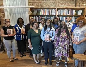 Group of young black women pictured with author Dr. Menah Pratt who is dressed in African print dress