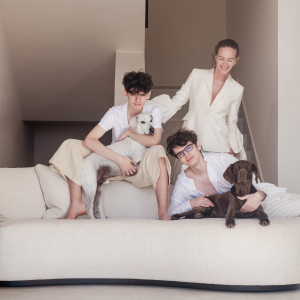 Woman poses with two teenage boys and two large dogs on beige couch.