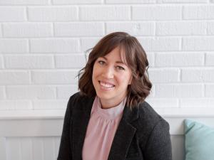 Jeana Atkison sits on a couch with a white brick wall in the background.