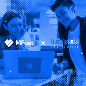 A man and a woman in an office setting looking at a laptop with a Vietnam flag sticker, representing the collaboration between MFast and Trusting Social.