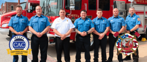 A group of Coweta Fire Department staff and officers in blue uniforms standing next to their fire truck.