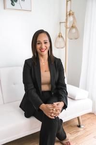 woman in black suit sitting on a couch looking at the camera and smiling with bright red lipstick