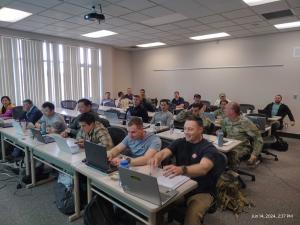 students sit at desks with computers in a PMP Prep Class at JBLM Army base