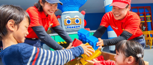 A diverse group of individuals joyfully engaging in Lego play at a bustling Legoland Japan Resort.