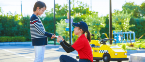 Woman handing a paper to a boy, both smiling.