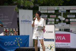 The Mayor of Toronto stands at a podium, addressing a crowd of cricket enthusiasts gathered at a local event. The background features banners and flags representing various cricket teams, with attendees visibly engaged and excited. The Mayor is seen smili