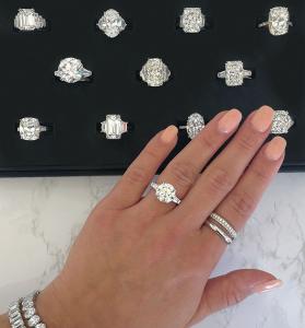Elegant diamond ring held by woman's hand near engagement ring collection.