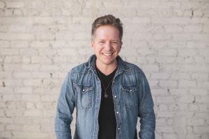 photo of Carl Cartee wearing a jean jacket standing in front of a brick wall