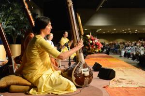 Nuns in yellow saris playing musical instruments on a stage in front of a crowd