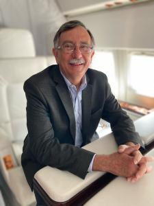A smiling man sits in an executive jet seat and smiles for the camera
