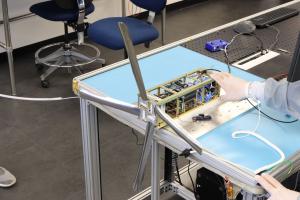 Image of D3 and IGOR satellite on top of table in the Axient Testing Facility. The D3 has it's 4 booms extended over the edge of the table.