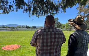 Two UAS pilots flying a drone at University of Montana in Missoula, MT with mountains visible in the background.