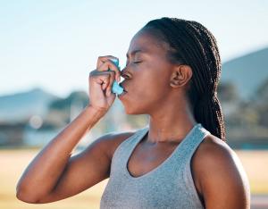Young black female athlete in tank top using inhaler outside