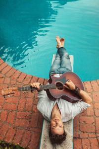 Dylan Galvin laying upside down by a pool with his acoustic taylor guitar.